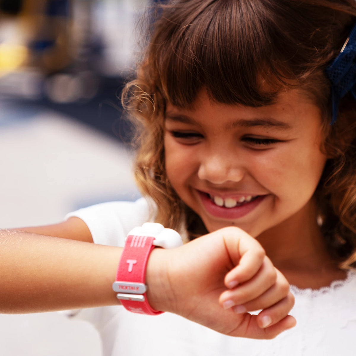 Girl smiling while wearing a red TickTalk kids smartwatch, representing the TickTalk brand story and family connection